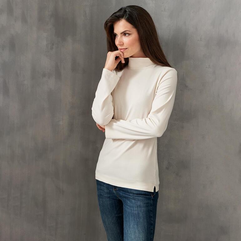 Frau in cremefarbenem Baumwoll/Kaschmir-Highneck-Shirt und Jeans.