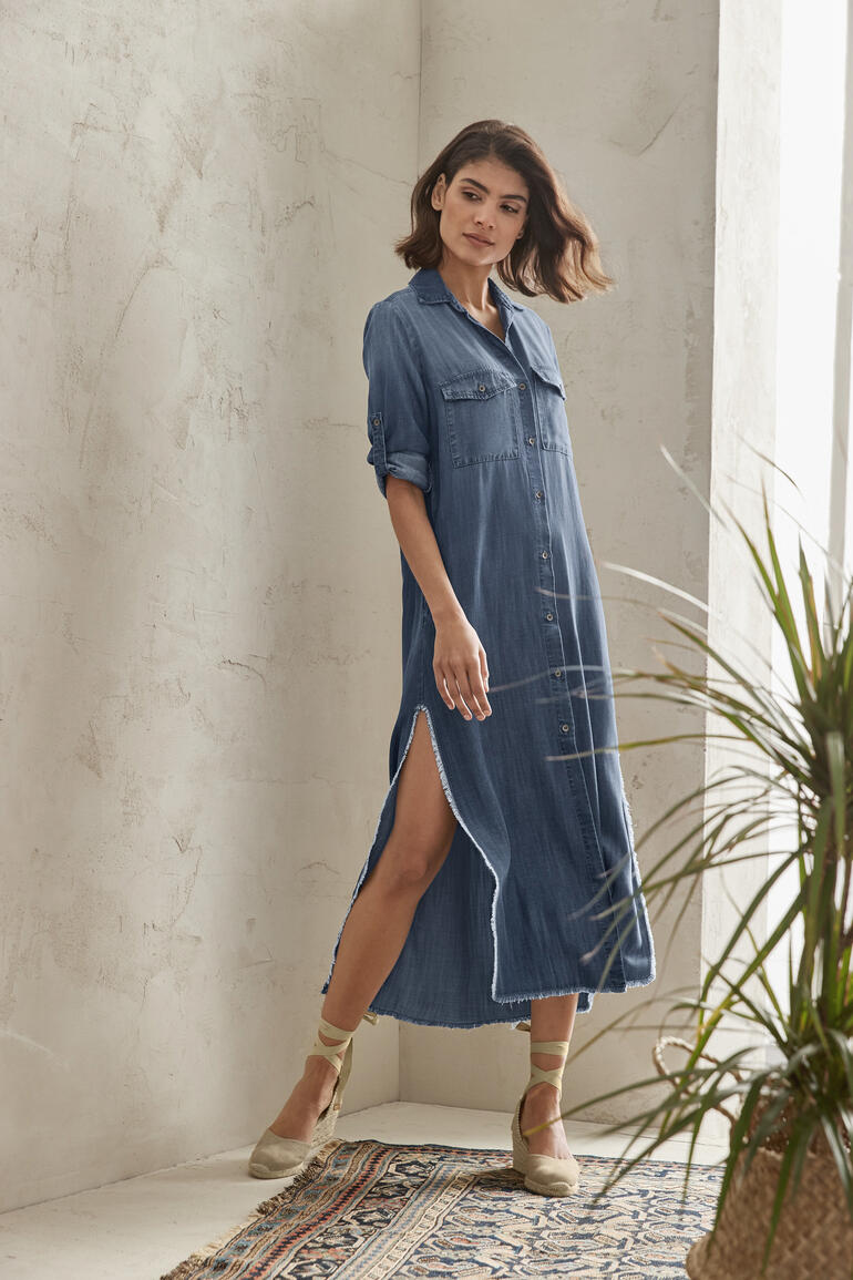 Frau in Jeansblusen-Kleid mit Schlitz steht in einer Pose.