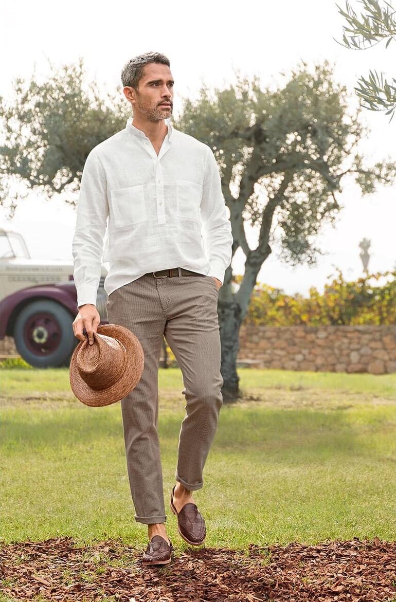 Gardeur Hahnentritt-Sommer-Chino Mann in leichten Leinenhemd mit einer Strohhut in einer mediterranen Umgebung.