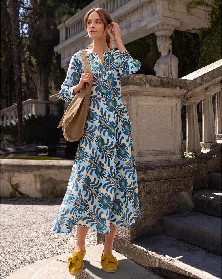 Curry Frau trägt ein Ikat-Kleid mit buntem Muster, steht auf einer Treppe im Freien.