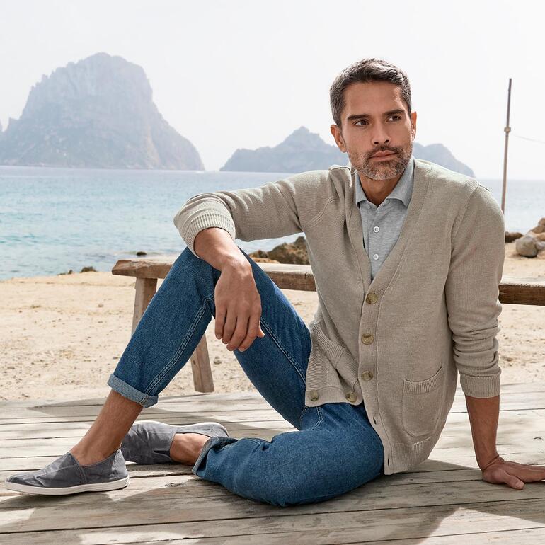 Grau Mann in beige Leinen-Cardigan sitzt am Strand