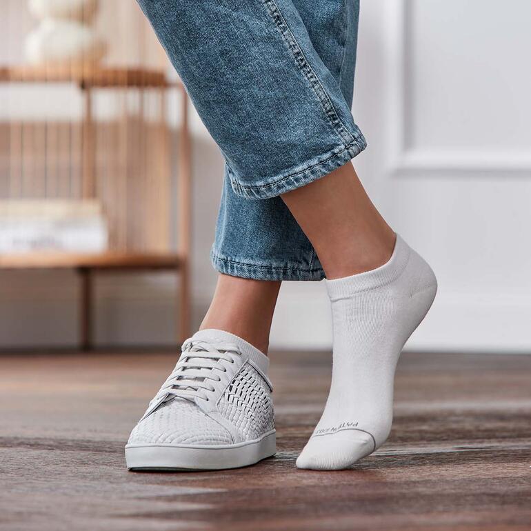 Weiss Füße in Sneakers mit einer weißen Sneakersocke, die auf einem Fuß sichtbar ist.