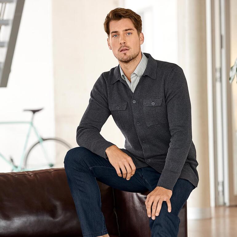 Mann sitzt auf einem Sofa, trägt eine graue Strickjacke.