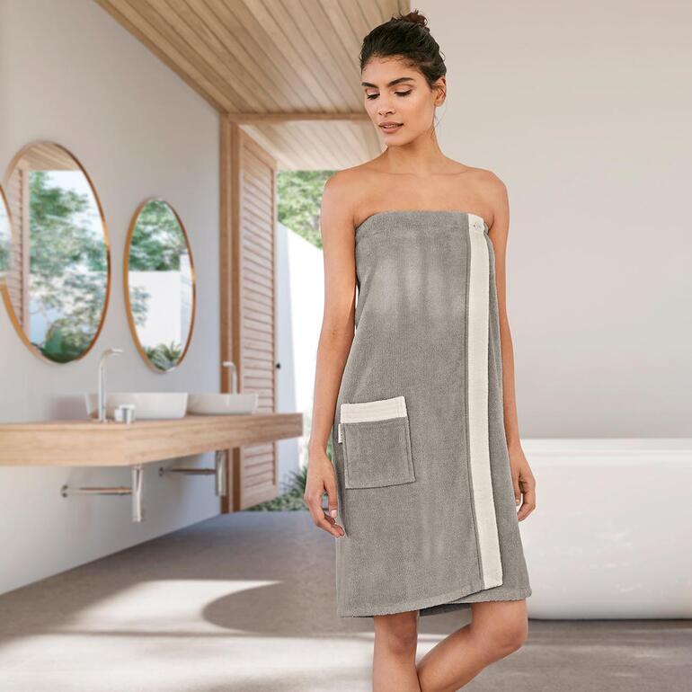 Frau in einem grauen Sauna-Sarong mit seitlicher Tasche in einem modernen Badezimmer.