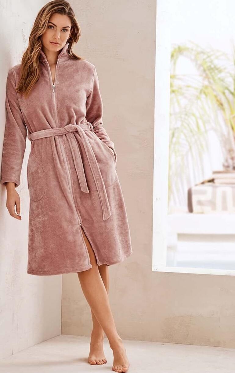 Peignoir Couture Frau in rosa Couture-Bademantel, stehend an einer Wand.