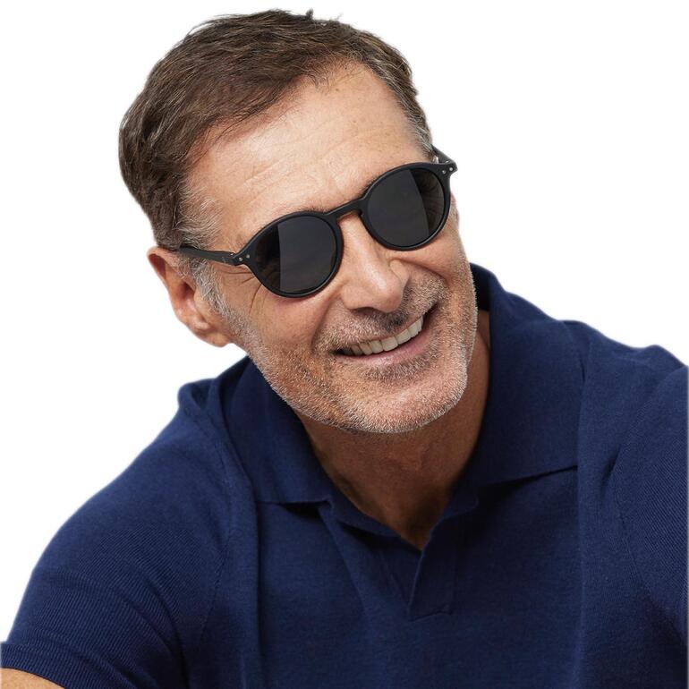Mann mit Sonnenbrille lächelt, trägt einen dunkelblauen Poloshirt.