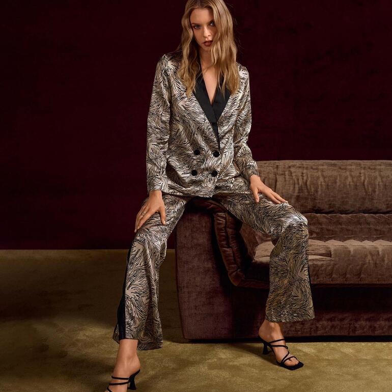 Frau in gemustertem Schlafanzug mit Jacke und Hose, sitzt auf einem Sofa.