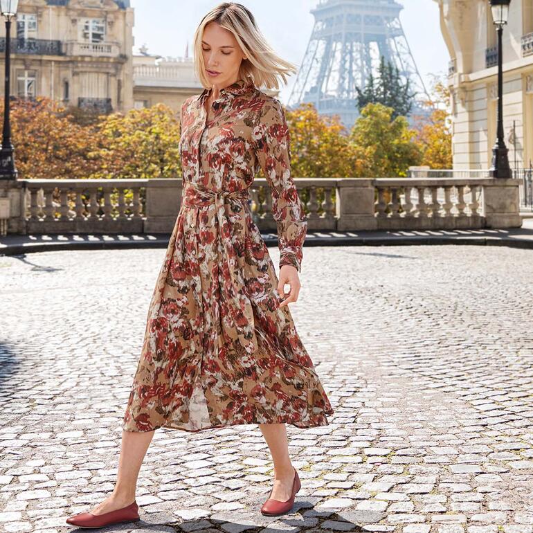 Frau in floralem Woll-Seiden-Kleid, geht auf einem Kopfsteinpflaster.