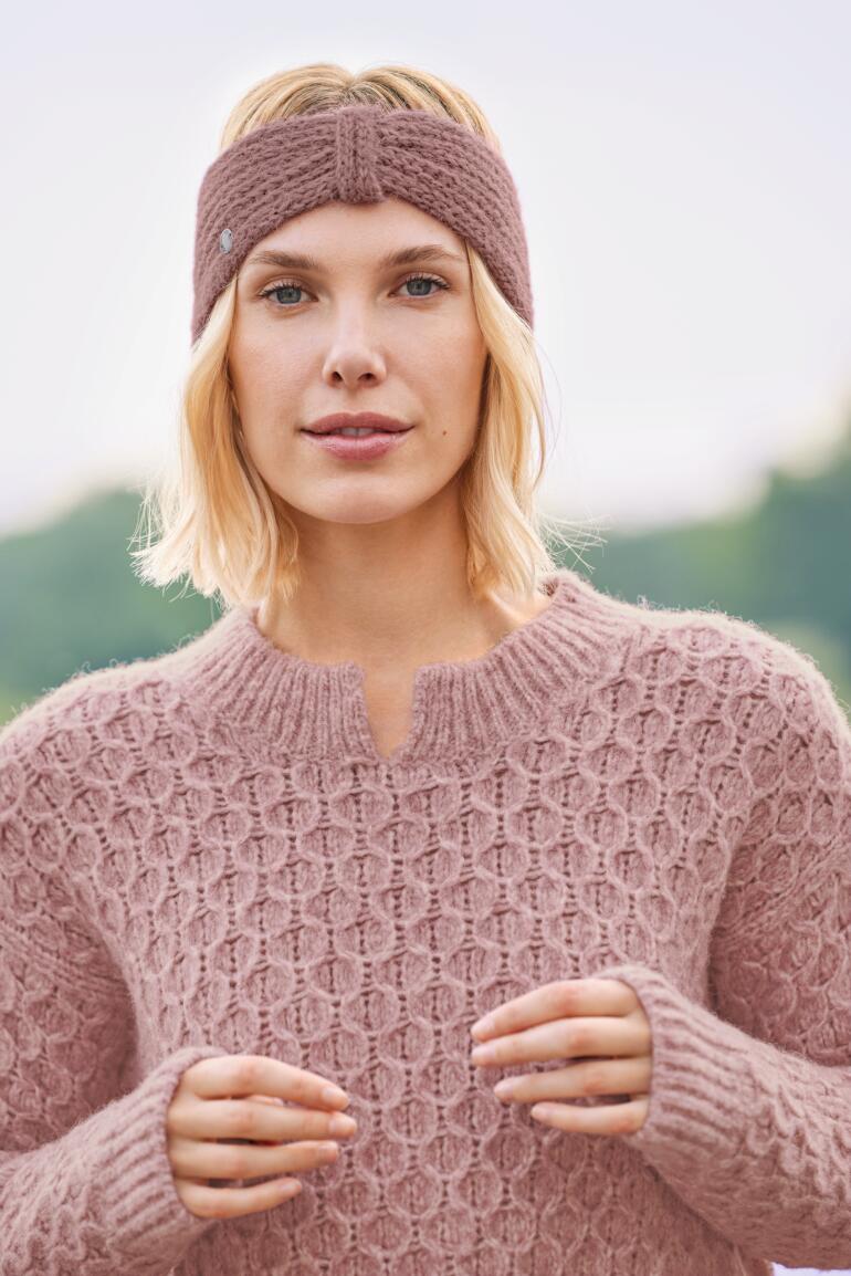 Beere Frau mit Alpaka-Stirnband in Rosa und Grobstrickpullover.