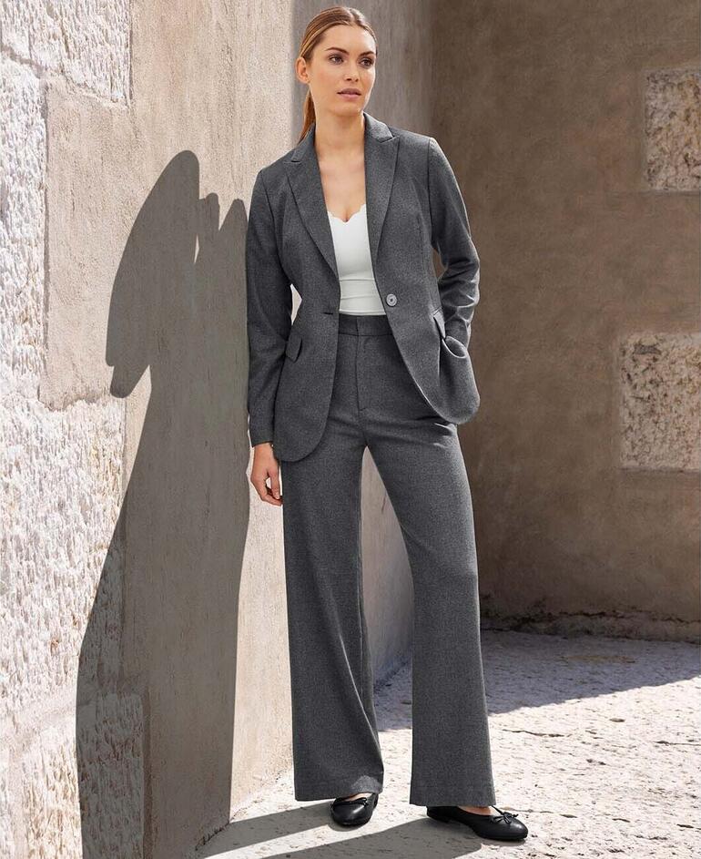 Blazer und Hose Frau steht in grauem Blazer und Hose an einer Mauer