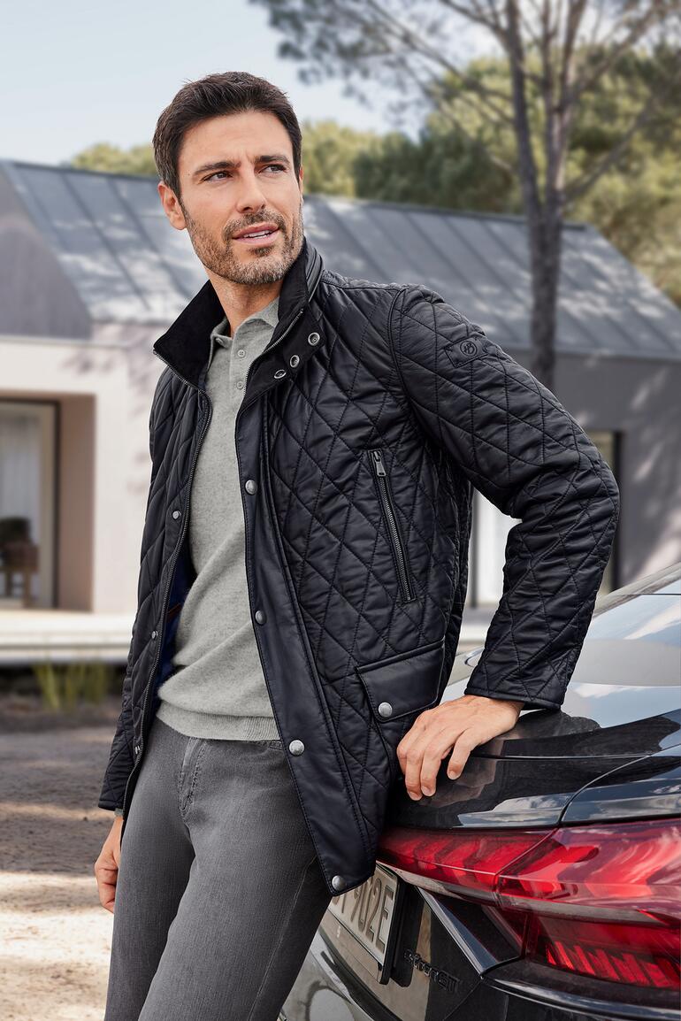 Heinz Bauer Lammnappa-Steppjacke Mann in schwarzer Steppjacke mit Lammnappa vor einem modernen Gebäude.