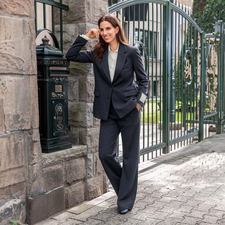 Frau in einem schwarzen Wolljersey-Blazer und -Hose vor einem historischen Gebäude.