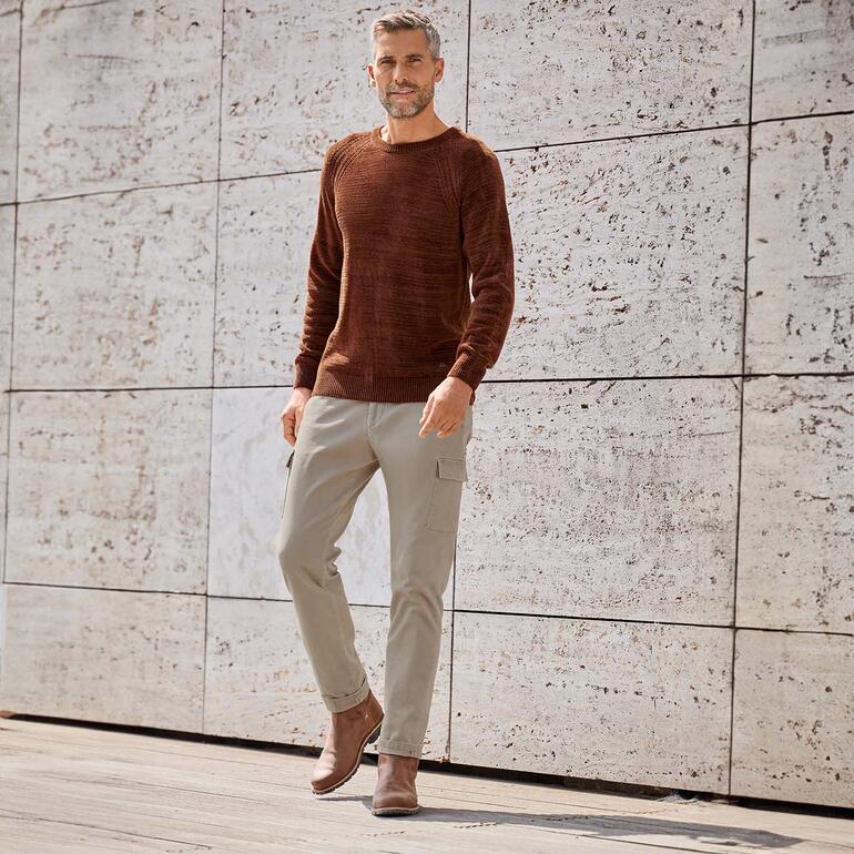Mann trägt braunes Pullover und beige Dobby-Cargo-Hose vor einer Strukturwand.