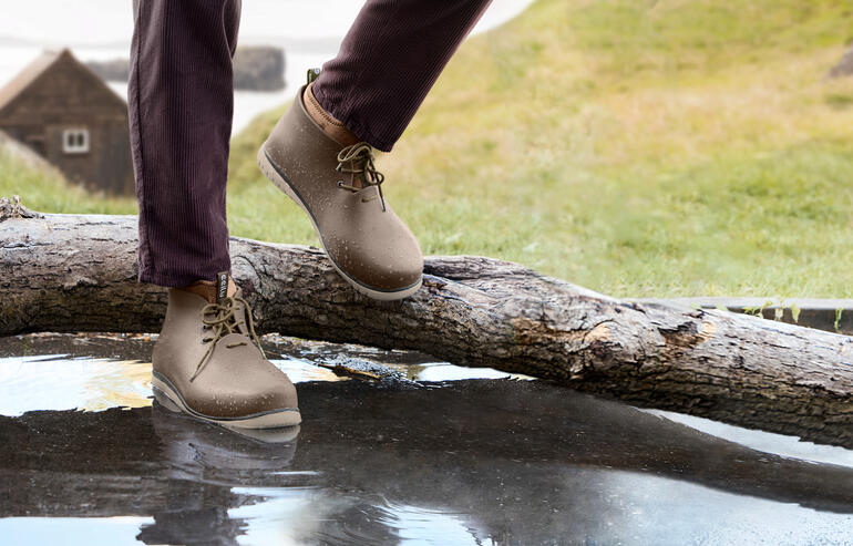 Mann trägt beige Ccilu Regenboots und steht neben einem Baumstamm auf Wasser.