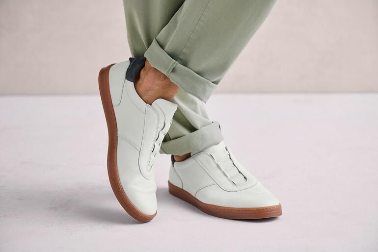 Weiss Mann trägt weiße OCONI Slip-on Schuhe auf grauem Untergrund.