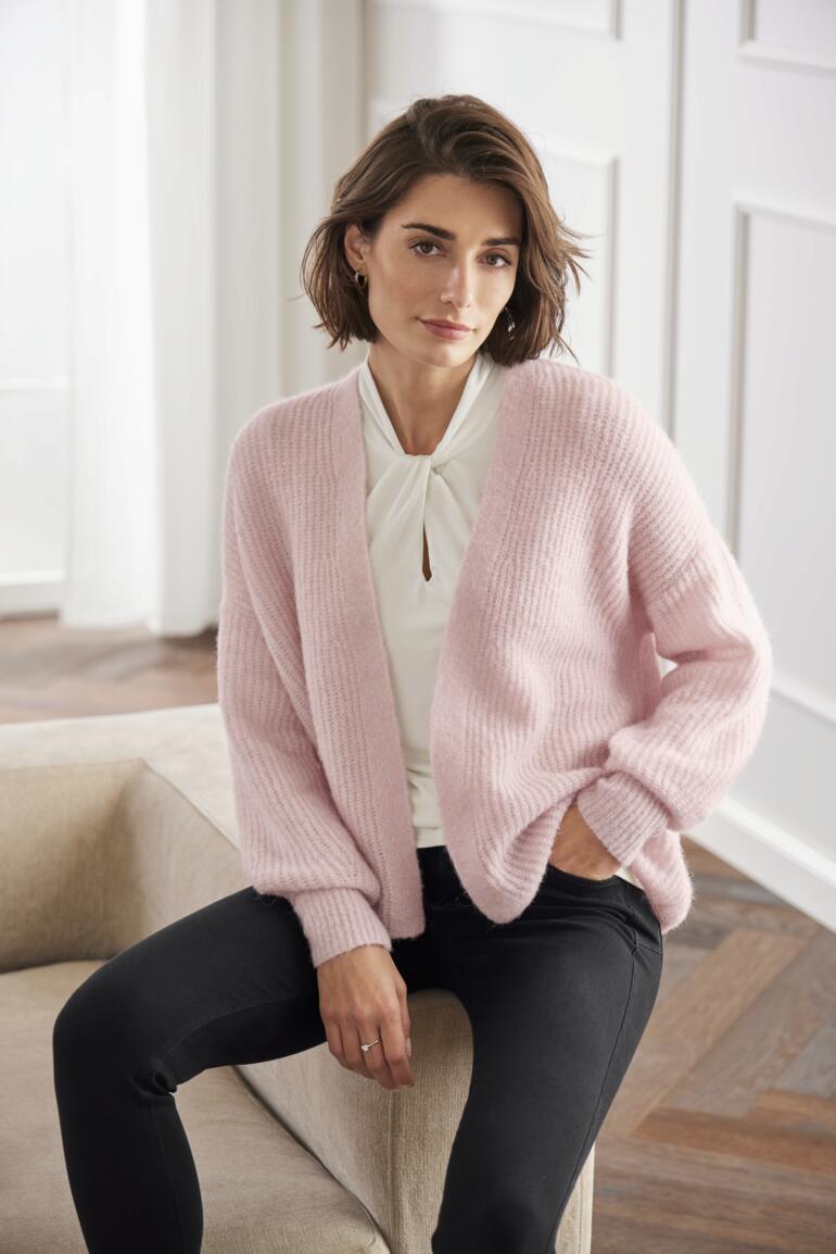 Frau sitzt im Junghans 1954 Flausch-Cardigan in rosa.