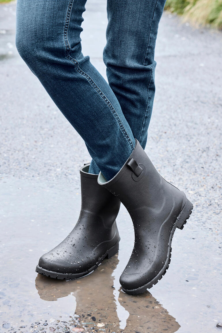 Schwarze Gummistiefel von Green Comfort, stehen in einer Pfütze.