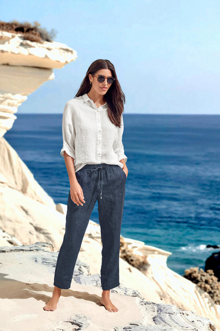 Gardeur Indigo-Leinen-Joggpants Frau in luftiger Bluse und Hose steht am Meer.