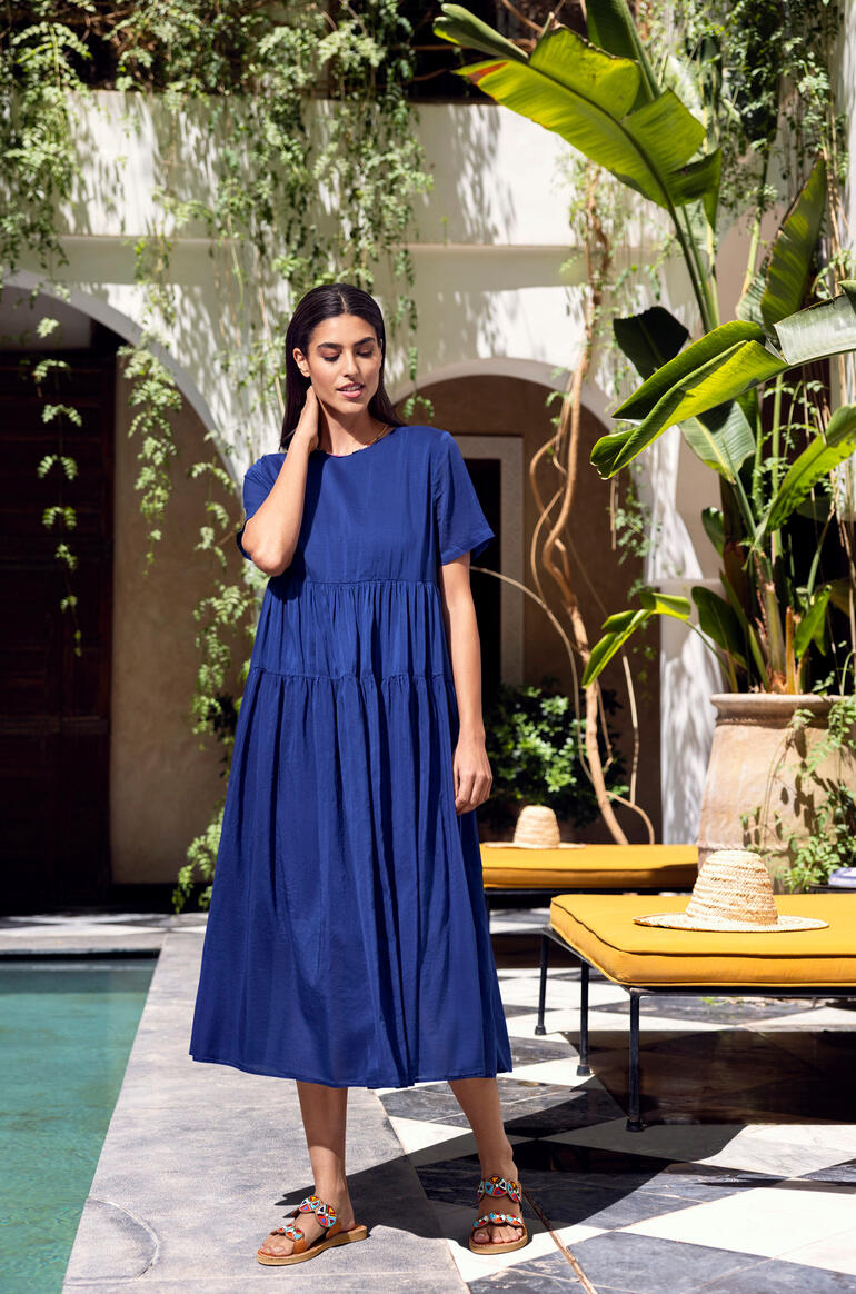 Frau in blauem Sommerkleid steht vor einer eleganten Kulisse