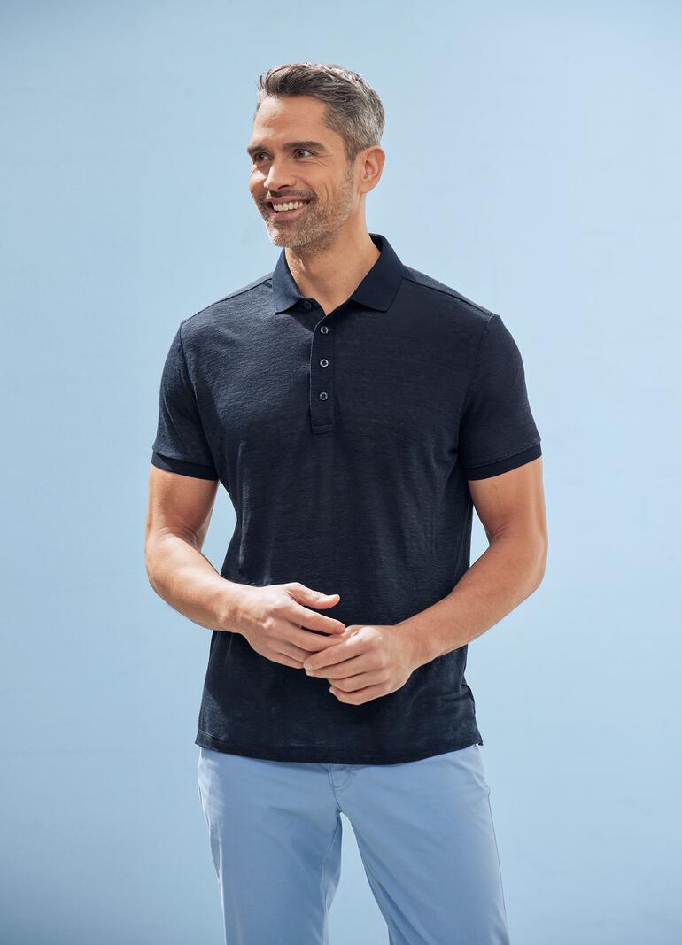 Schwarz gekleideter Mann mit dunkelgrau-blauem Polo auf blauem Hintergrund.
