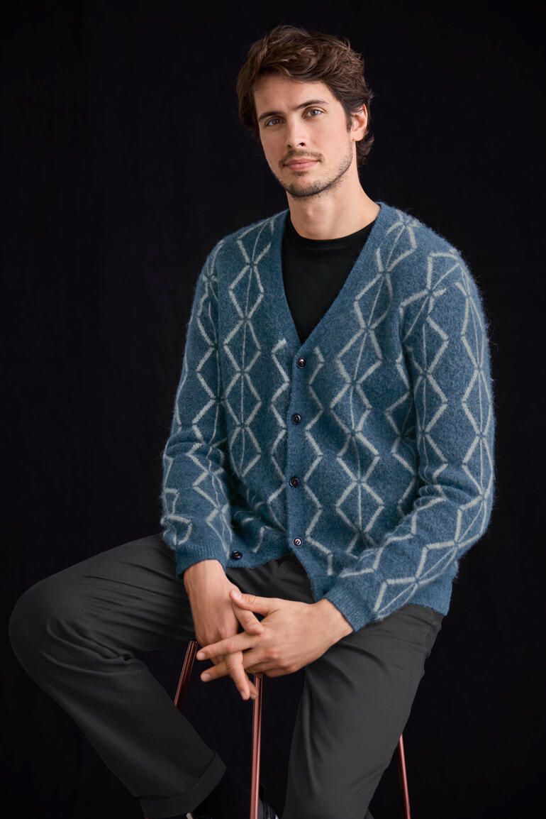 Mann sitzt in einem blauen Brushed-Alpaka-Cardigan mit Rautenmuster.