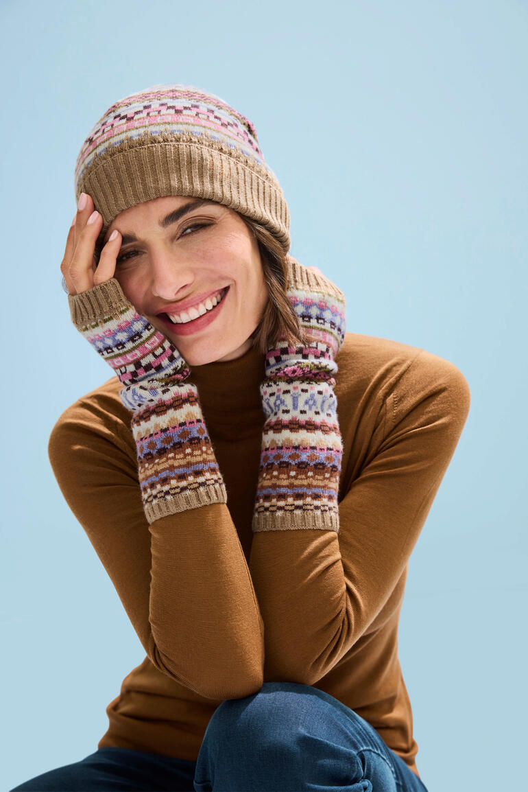 Frau trägt Jacquard-Mütze und Stulpen, lächelt in winterlicher Umgebung.