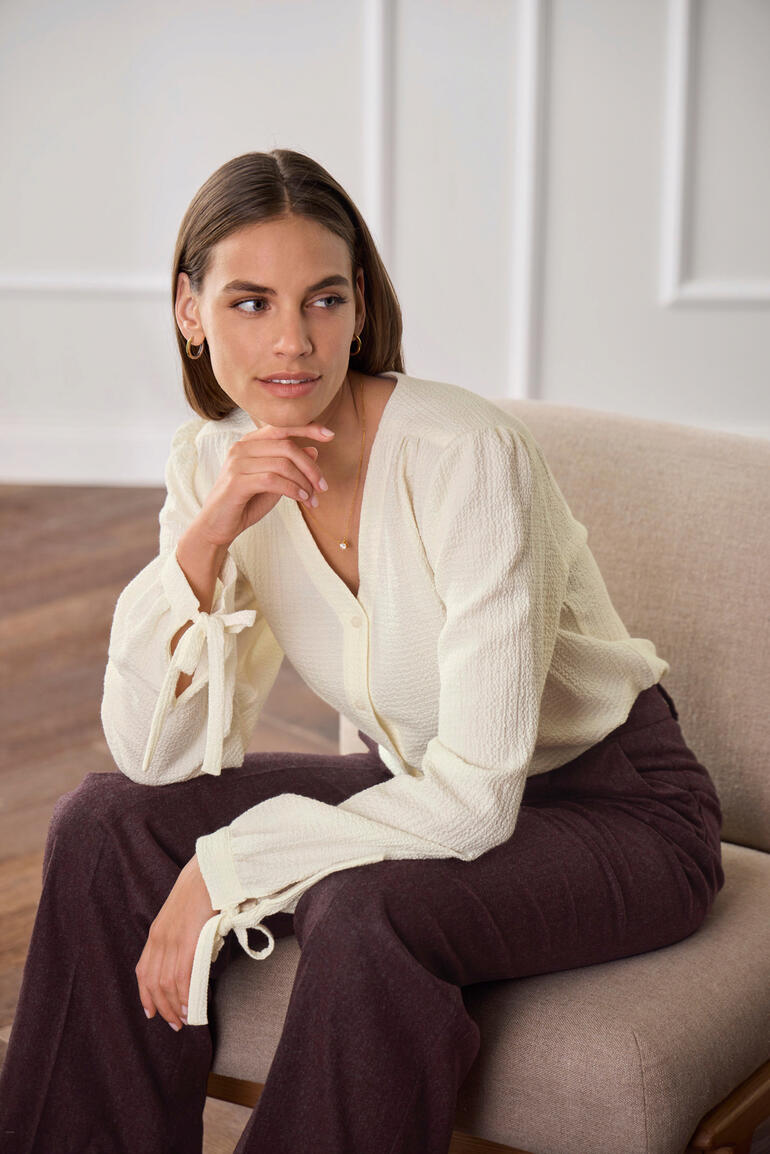 Frau sitzt in einer hellen Baumwoll-Kaschmir-Bluse mit gebundenen Ärmeln.