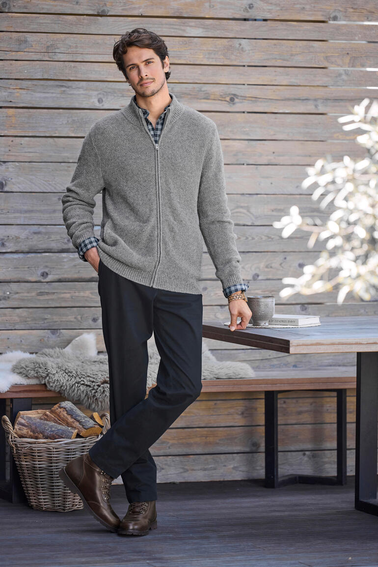 Mann in einer grauen Alpaka-Klima-Strickjacke vor einer Holzwand