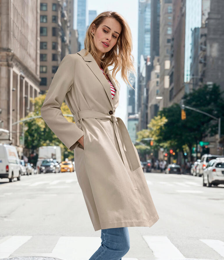 Frau in beigem Alpaka-Seiden-Mantel auf einer belebten Stadtstraße.