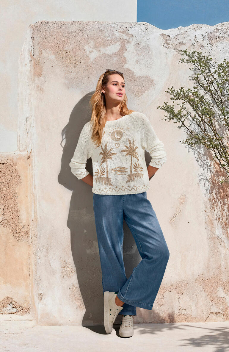 Bella Dahl Wide-leg-Jeans Frau in cremefarbenem Pullover und hellblauen Wide-leg-Jeans, vor einer Wand.