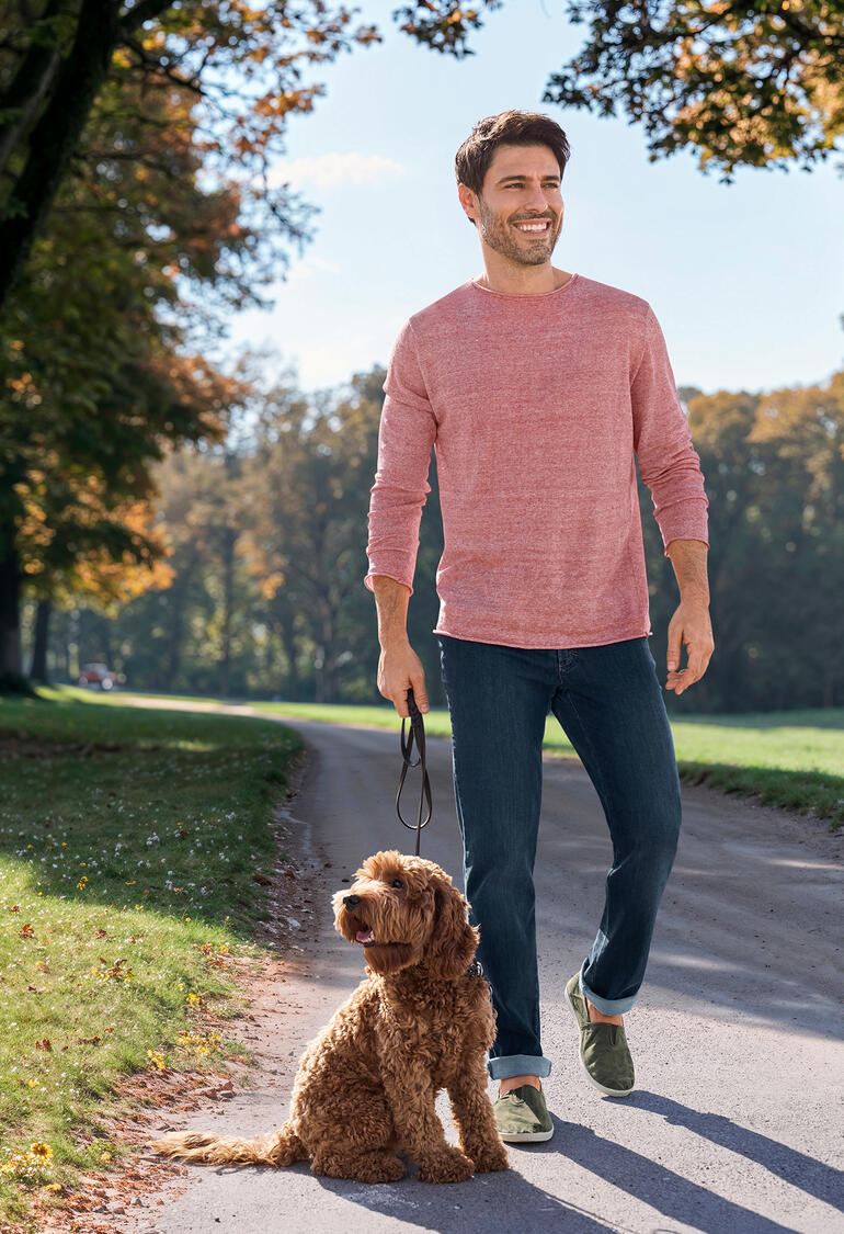 Rot/Natur Mann in einem rosanen, leichten Pullover, geht mit einem Hund auf einem Weg.