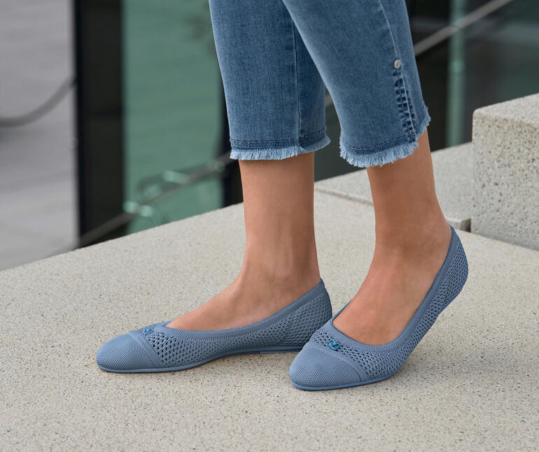 Frau trägt blaue Mesh-Ballerinas, steht im Freien auf Steinboden.