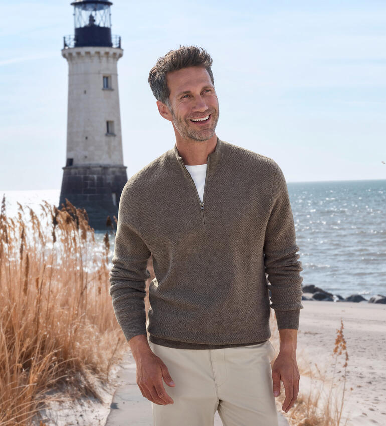 Junghans 1954 Kaschmir-Piqué-Troyer Mann trägt einen Pullover an einem Leuchtturm am Meer