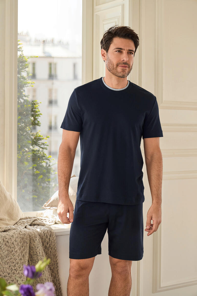 Recovery Pyjama Mann steht in einem hellen Raum in einem navy-farbenen Recovery-Pyjama mit kurzen Hosen.