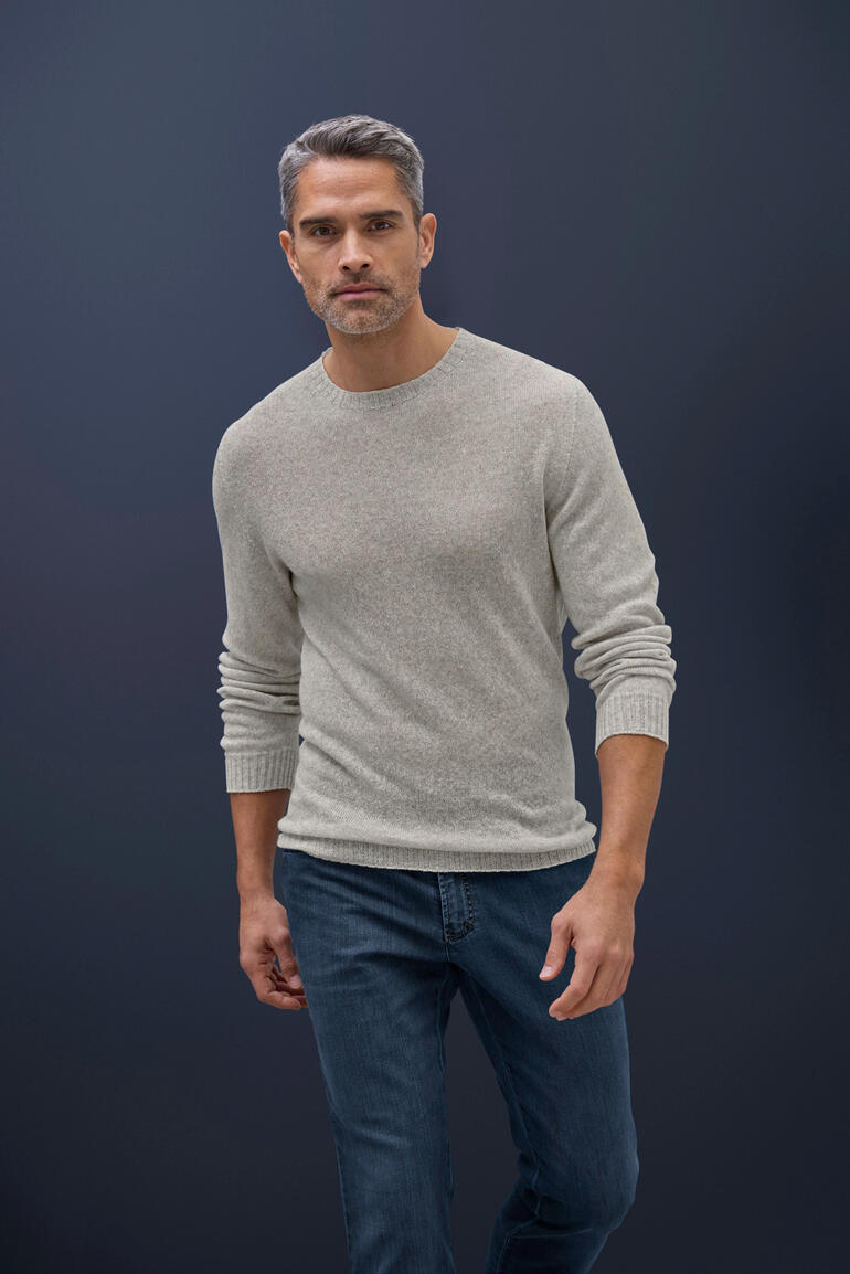 Mann trägt einen hellgrauen Kaschmir-Leinen-Pullover und Jeans vor dunklem Hintergrund.