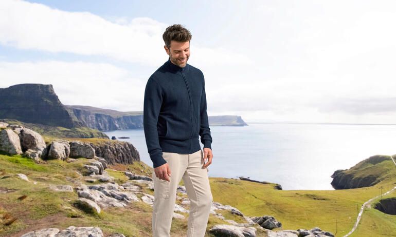 Mann trägt einen navyfarbenen Seiden-Klima-Cardigan, stehend vor einer Küstenlandschaft.
