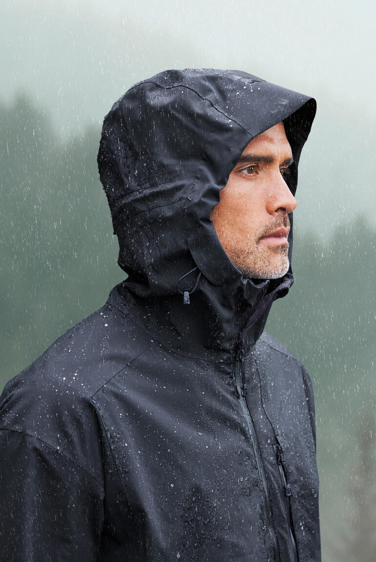Mann trägt schwarze Hardshell-Jacke mit Kapuze im Regen.