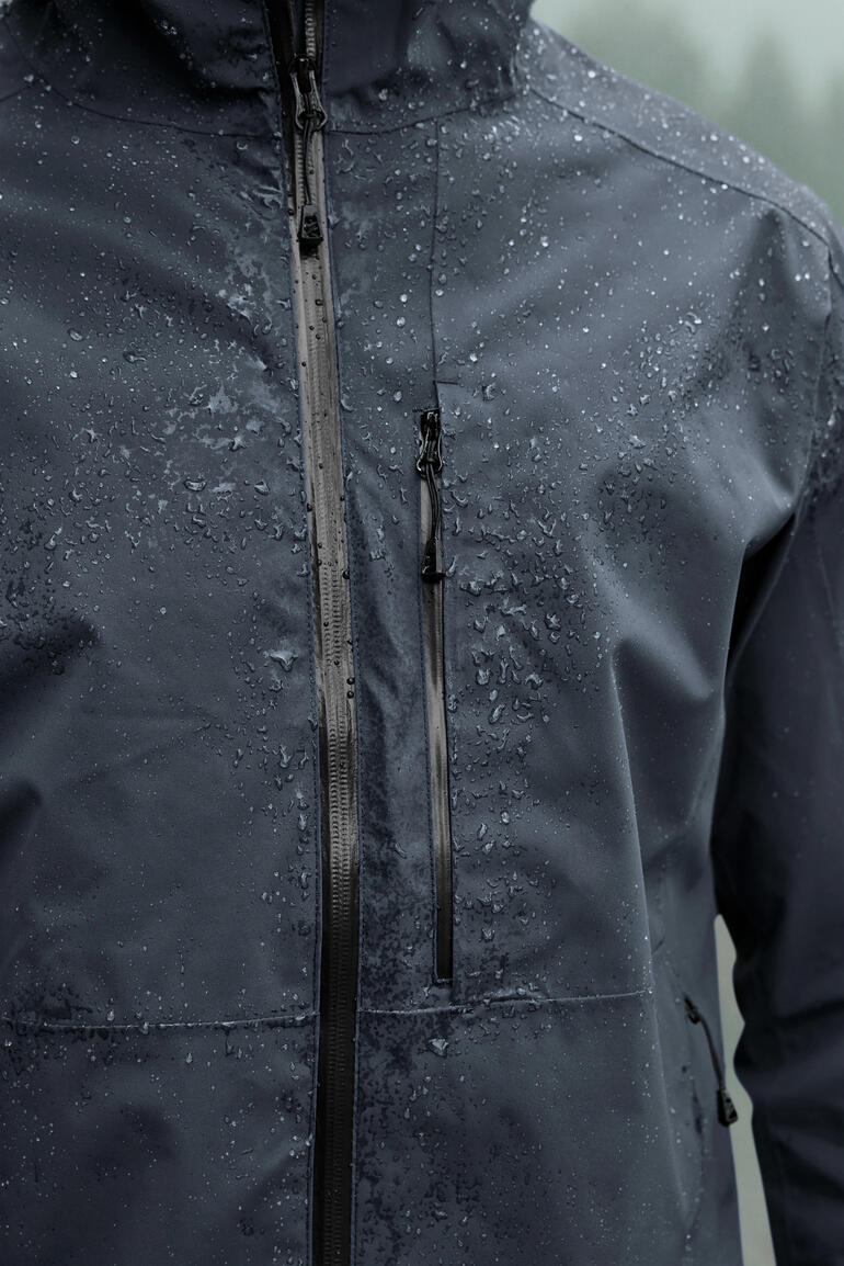 Nahaufnahme der grauen Hardshell-Jacke mit Regentropfen auf dem Stoff.