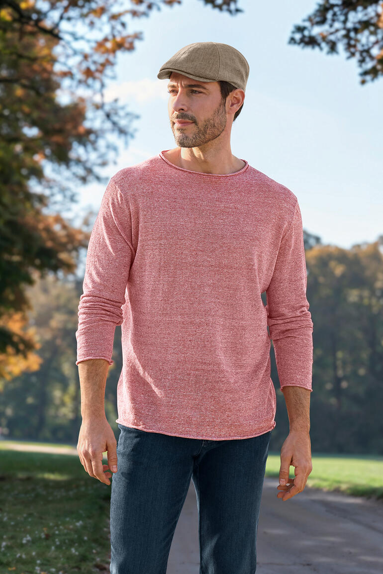 Mann in roten Pullover mit Longsleeve und Mütze in der Natur.