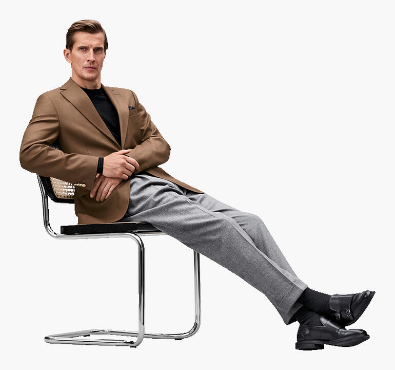 Mann sitzt in braunem Blazer auf einem Stuhl mit lässiger Pose.