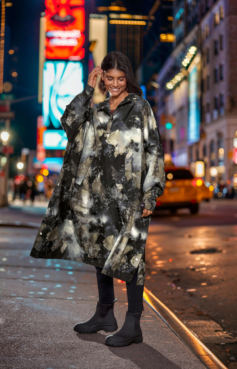 Poncho de pluie design Ilse Jacobsen Frau trägt ein gemustertes Regenponcho in einer Stadt bei Nacht.