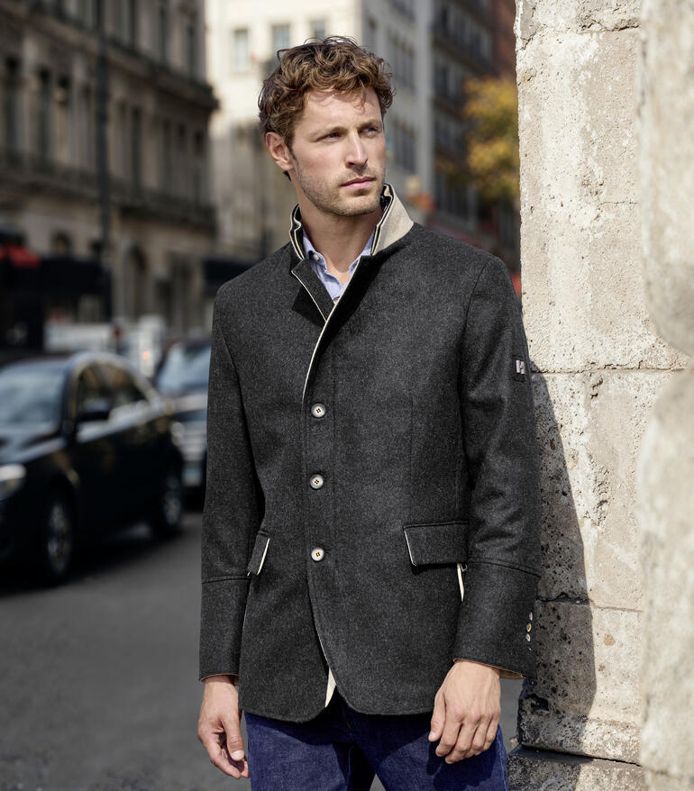 Mann in Merino-Lodenjacke steht an einer Wand in der Stadt