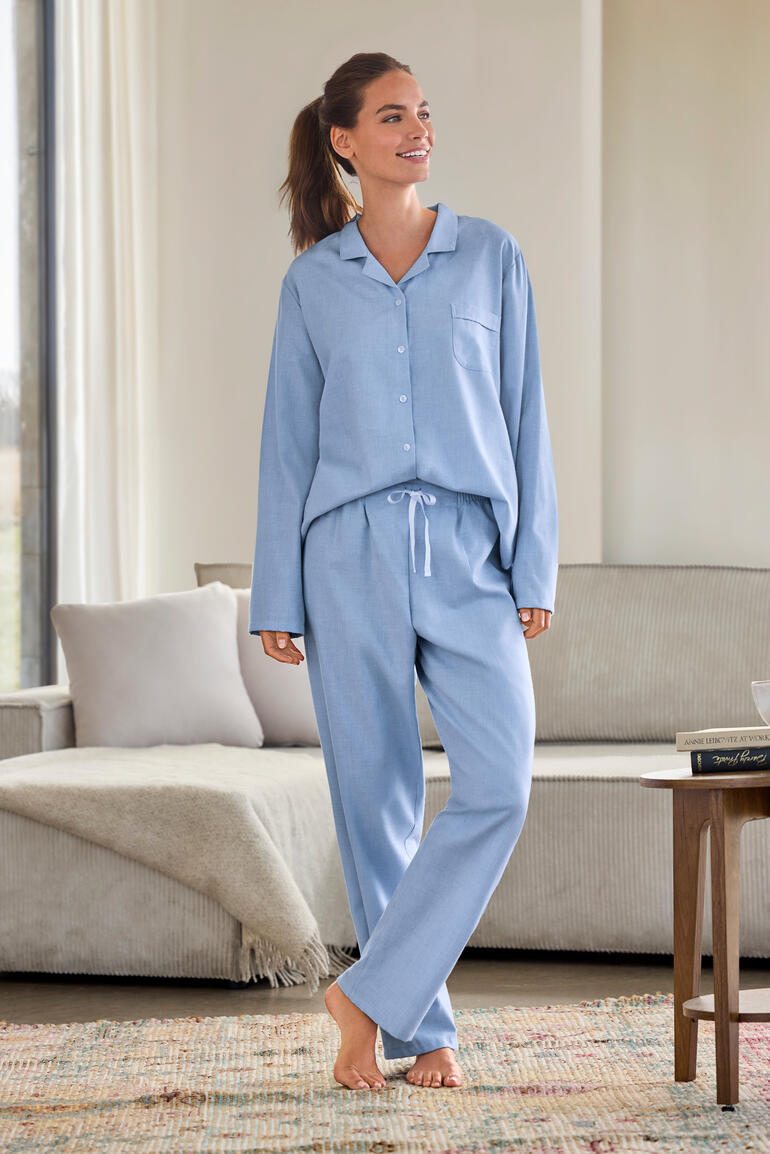 Frau in blauen Woll-Flanellpyjama, steht im Wohnzimmer mit entspannter Pose.