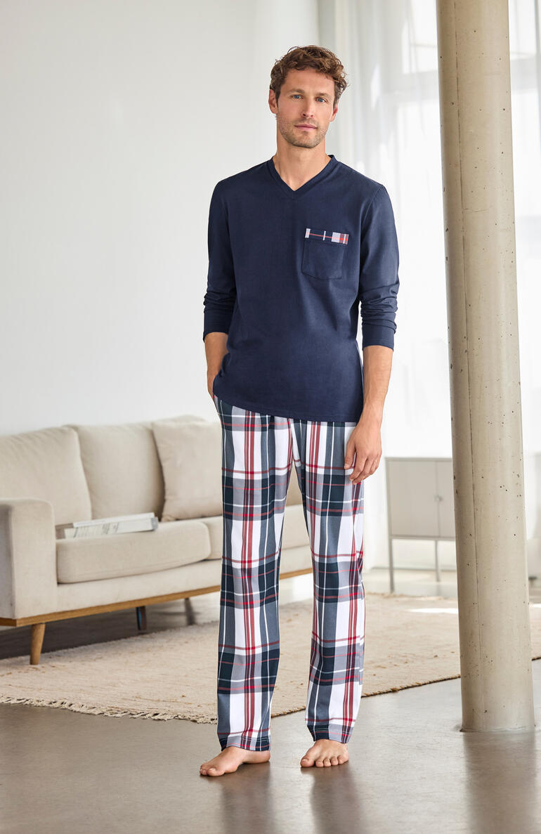 Mann in einem blauen Karo-Pyjama mit Hose steht in einem Wohnzimmer.