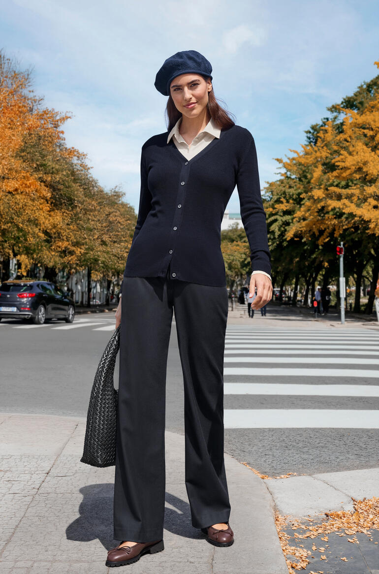 Navy Frau in dunkelblauer Strickjacke und schwarzer Hose in herbstlicher Umgebung.