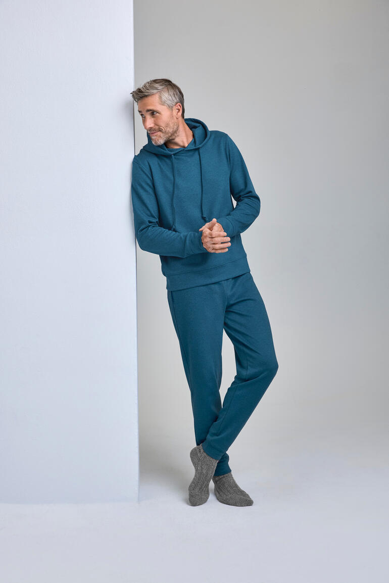 Mann in tealfarbigem Cashmere-Cotton Loungewear-Anzug lehnt an Wand.