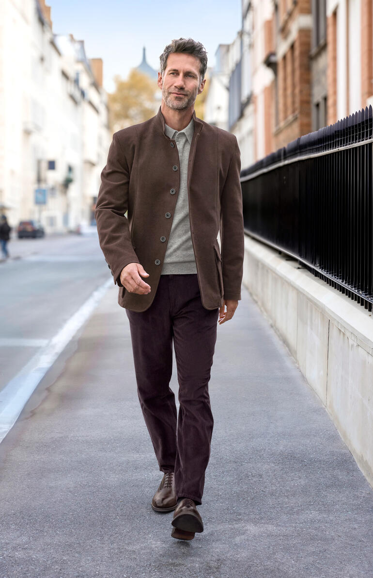 Raisin Mann in einem braunen Moleskin-Jacket geht in einer urbanen Umgebung