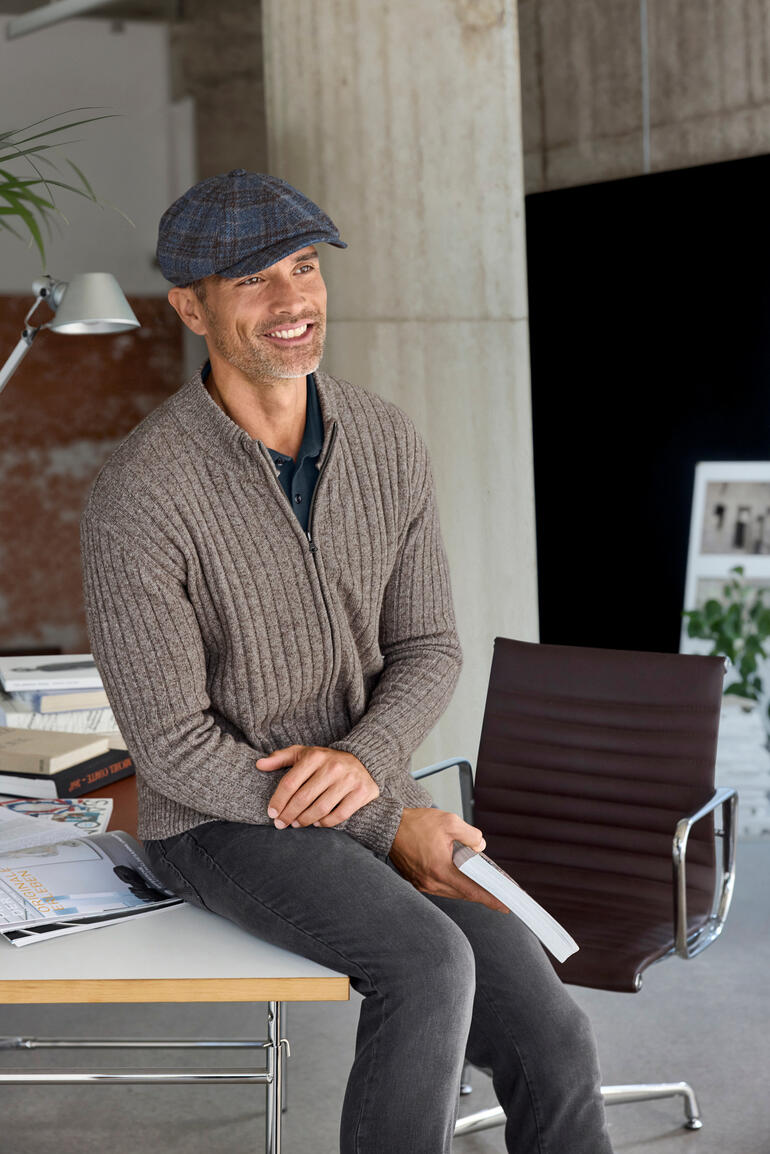 Paperboy Cap Mann in grauem Pullover mit Papierhut, lächelnd am Tisch sitzend, Größe 56