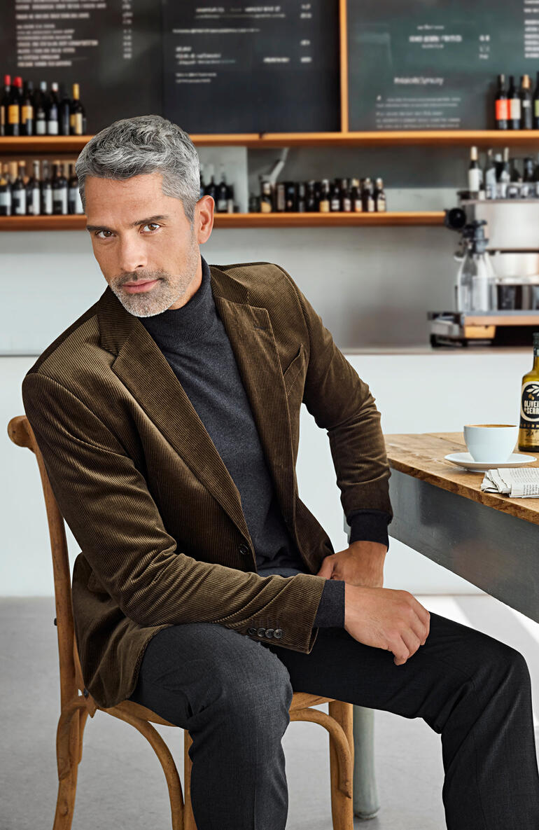 Mann in braunem Cord-Sakko sitzt in einem Café mit einem eleganten Look.