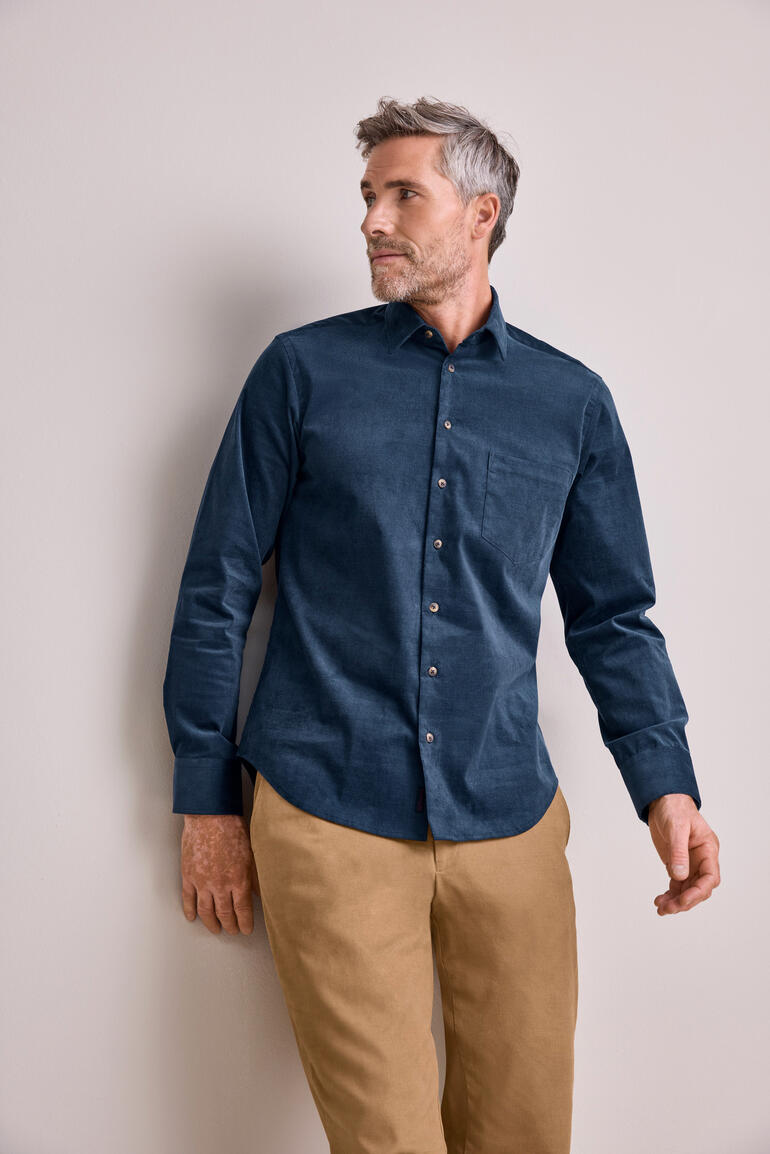 Mann in dunkelblauem Cordhemd mit beigefarbener Hose.